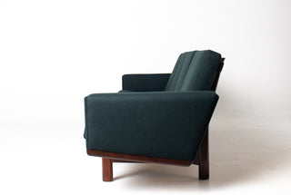 Close-up of the sculpted arm and rear teak frame on a Hans Wegner GE-236 sofa upholstered in Maharam Gemma Caliber dark green wool fabric.