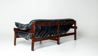 A mid-century modern wooden sofa with a black leather tufted seat and backrest, shown from a three-quarters angle against a plain white studio background.