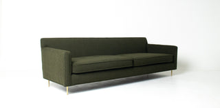 An olive green upholstered three-seater sofa with slim gold metal legs, shown from a three-quarter angle against a plain white studio background.