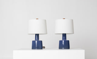 Pair of Gordon and Jane Martz Marshall Studios cobalt blue ceramic table lamps with white drum shades and teak finials, displayed on a white pedestal