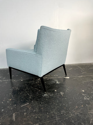 A blue upholstered Paul McCobb 312 Armchair with a black lacquer maple wood base, viewed from an angle that highlights the chair's profile.