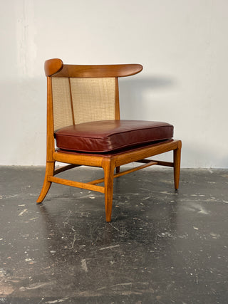 A vintage Tomlinson lounge chair with a caned backrest and cushioned seat, featuring a wooden frame and rear legs, and a brown cushion.