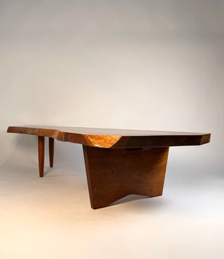 Profile of George Nakashima conoid coffee table showing the gently sloped English walnut tabletop the natural live edge as supported by sculptural leg base beneath.